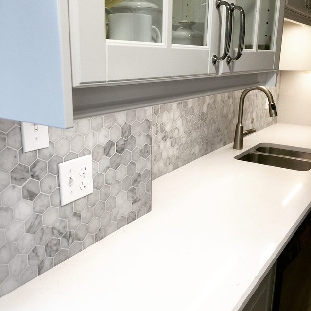 Marble-look hexagon backsplash with clean cuts around an outlet and window trim
