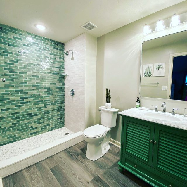 Walk-in shower with green glass subway tile, white tile curb and wood-look plank tile floor